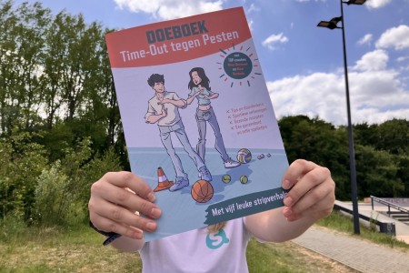 Iemand met een Sportieq-t-shirt aan houdt het Doeboek Time-Out tegen Pesten voor zich uit.